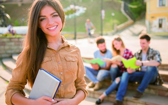 Schülerinnen und Schüler an die Hochschulen Mädchen hält ein Buch in der Hand, im Hintergrund sind drei Studierende